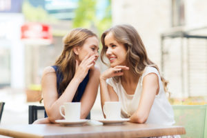 young women drinking coffee and talking at cafe